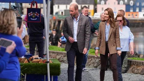 PA Media William and Kate look at an RNLI stall with the coloured houses of Tobermory behind them